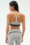 A woman stands with her back to the camera, wearing the SPLITS59 Emerson Airweight Bra in Dove Grey/Indigo and matching high-waisted leggings, perfect for hot yoga or Pilates.