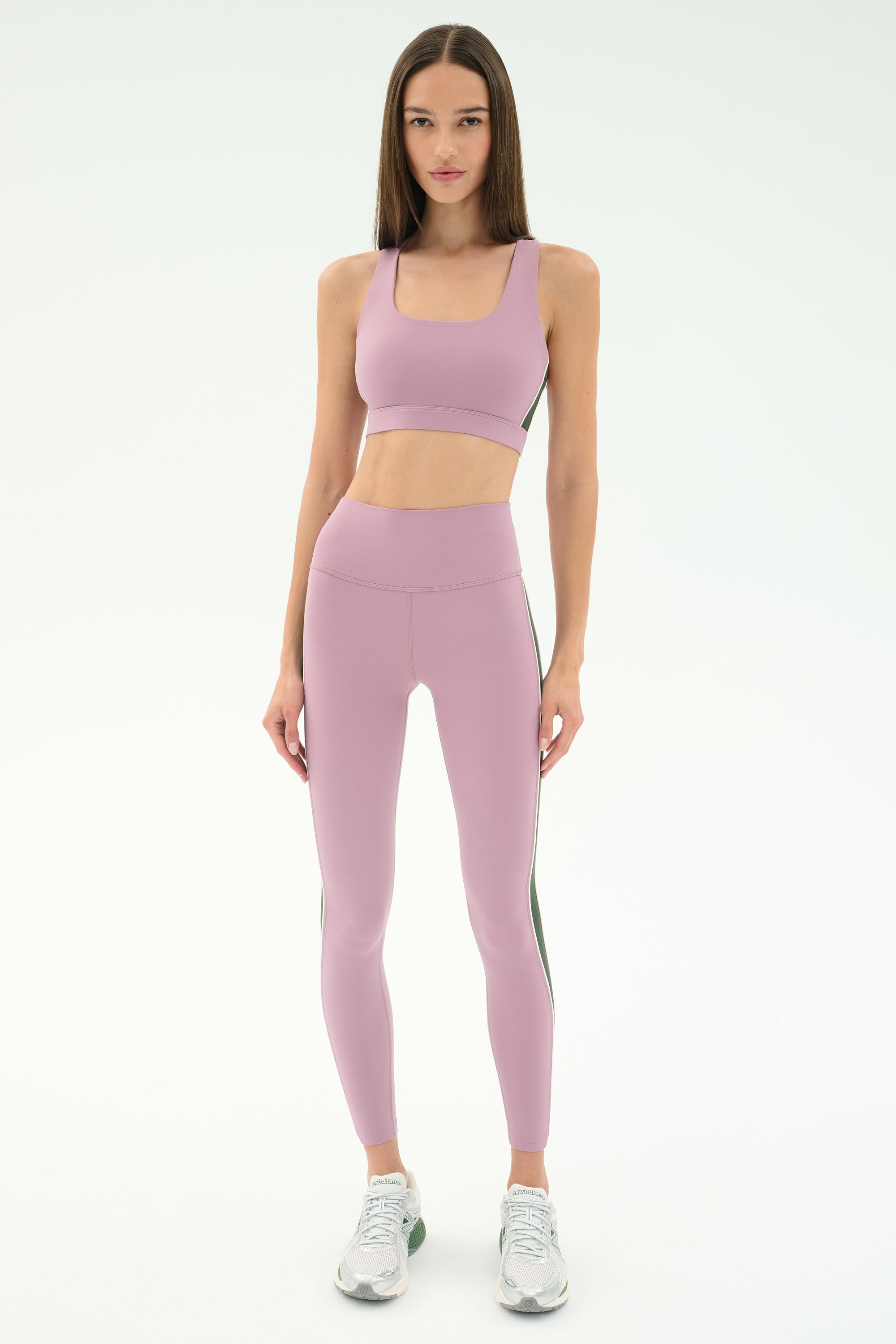 A woman faces forward, wearing the SPLITS59 Lexi Rigor Bra in Blush/Military paired with matching leggings and white athletic shoes, set against a plain light background.