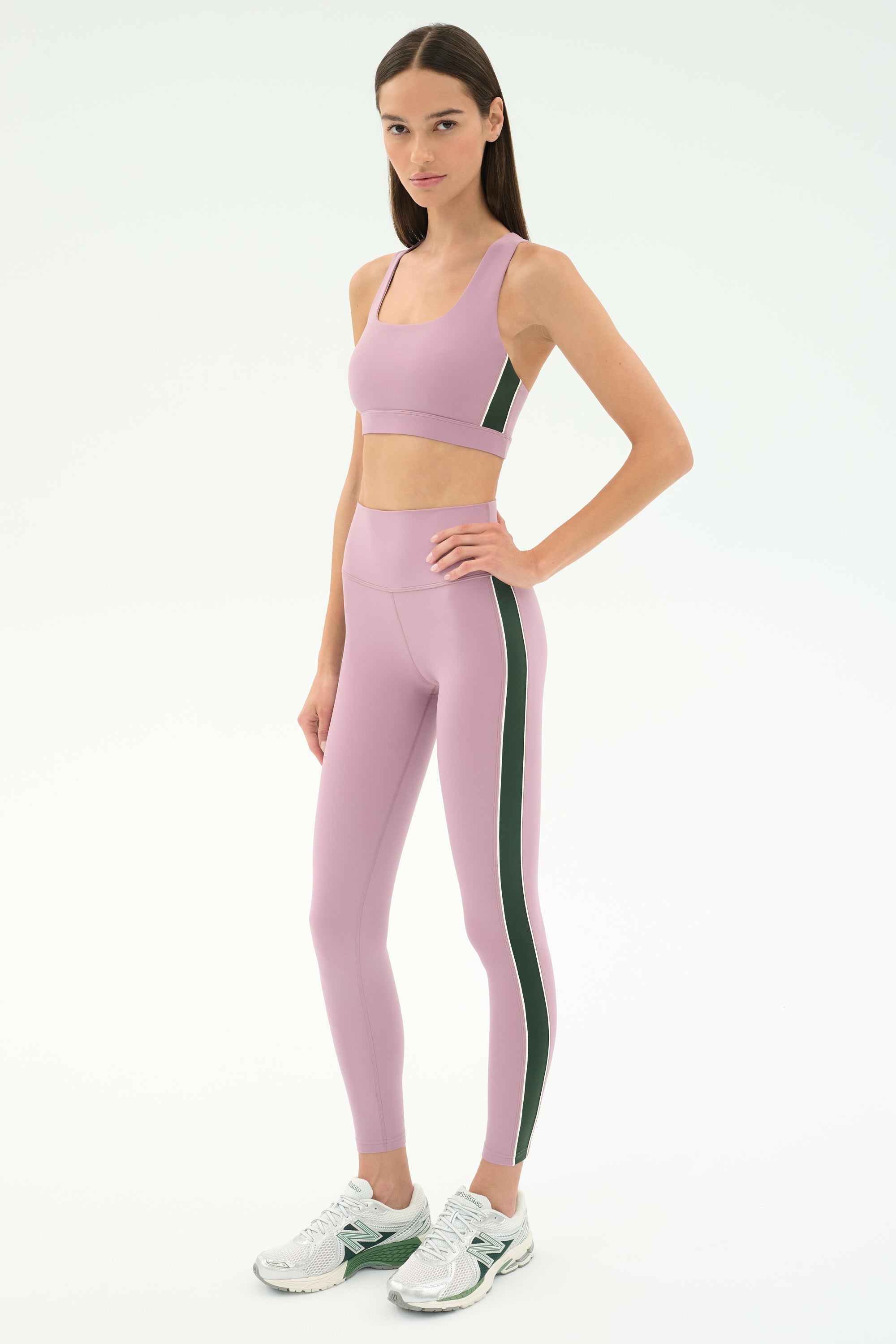 A woman wears the SPLITS59 Lexi Rigor Bra in Blush/Military with matching leggings and white sneakers, standing against a plain white background.
