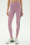 A person wears SPLITS59 Margot Rigor Legging in Blush/Military—mauve leggings with a dark green side stripe—paired with white sneakers, standing against a plain white background.