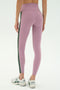 A person wearing SPLITS59 Margot Rigor Legging in mauve with a dark green side stripe and white New Balance sneakers, shown from the back against a plain background.
