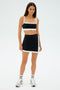 Sporting SPLITS59's Monah Rigor Bra in black/white, the person stands against a white backdrop in sneakers and striped socks—ideal for retro vibes or a gym workout.