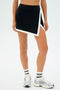 Person wearing the Monah Rigor Skort in Black/White by SPLITS59, paired with white socks and silver sneakers, against a plain background.