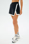 Someone wearing the SPLITS59 Monah Rigor Skort in black/white with matching socks and silver running shoes stands against a plain background.