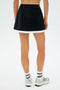 Someone is standing facing away, wearing the SPLITS59 Monah Rigor Skort in Black/White, paired with white socks and silver sneakers.