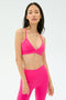 A woman stands facing forward, wearing the SPLITS59 Theo Rigor Bra in Berry, paired with matching leggings, against a plain light background.