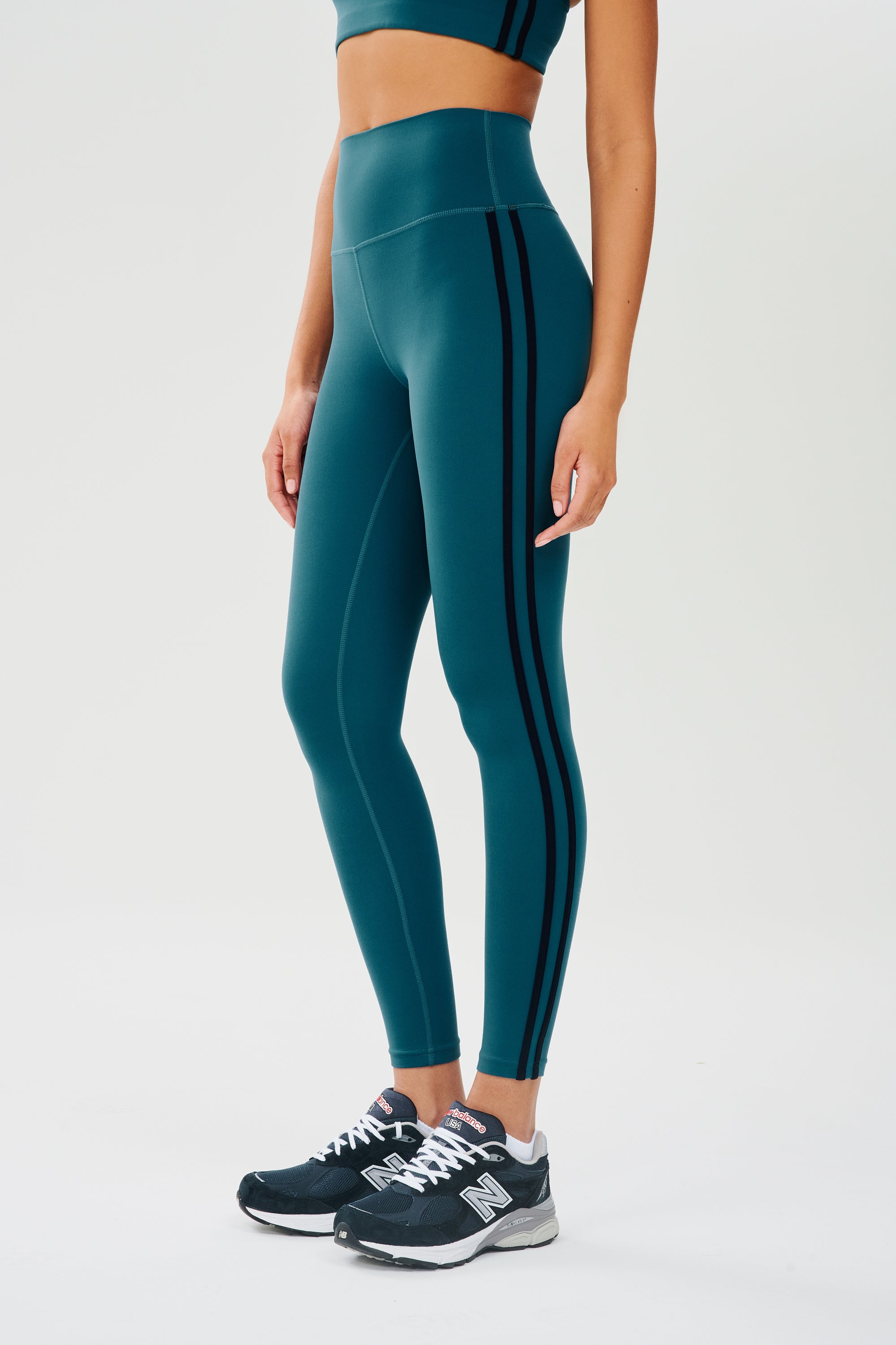A woman in SPLITS59 Ella High Waist Airweight 7/8 - Peacock/Indigo sports leggings.