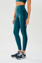 A woman in SPLITS59 Ella High Waist Airweight 7/8 - Peacock/Indigo sports leggings.