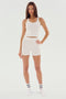 A woman stands wearing a white tank top, SPLITS59 Theo Rib Short - White for tailored comfort, and white socks with black stripes, set against a plain background.