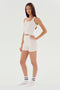 A person stands facing the camera, wearing a white tank top and matching Theo Rib Short - White by SPLITS59 with white socks. The background is plain white, highlighting the tailored comfort and classic design of the outfit.