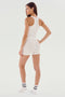 A person wearing a SPLITS59 Theo Rib Short - White, white tank top, white shorts, and white socks stands facing sideways with one hand on their hip, looking back over their shoulder. The background is plain white.