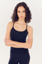A young woman with curly hair wearing a SPLITS59 Airweight Tank in Indigo and leggings stands with her arms crossed, looking directly at the camera against a white background.