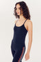 A woman with curly hair wearing a black full-length SPLITS59 support tank top and leggings with orange and white stripes, standing against a white background.