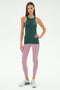 A woman stands against a white background wearing the SPLITS59 Kiki Rib Tank Full Length in Military, light purple yoga leggings with a dark stripe, and white sneakers.