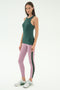 A woman stands against a plain background wearing the SPLITS59 Kiki Rib Tank Full Length in Military, light pink yoga leggings with a side stripe, and white athletic shoes—ideal for running or CrossFit workouts.