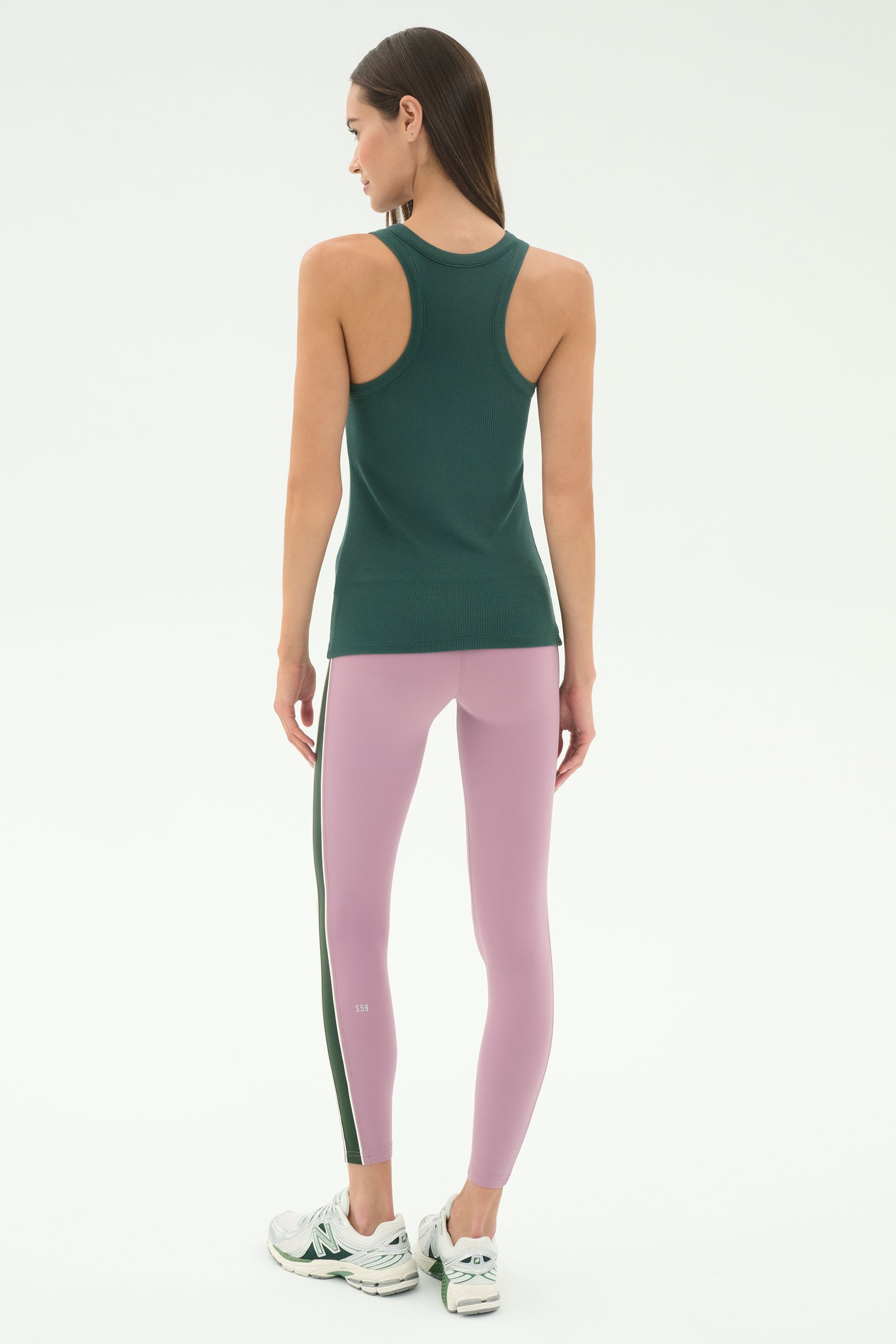 A woman faces away, ready for yoga or running in the SPLITS59 Kiki Rib Tank Full Length - Military, light purple leggings with a dark stripe, and white running shoes against a plain light background.