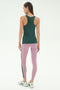 A woman faces away, ready for yoga or running in the SPLITS59 Kiki Rib Tank Full Length - Military, light purple leggings with a dark stripe, and white running shoes against a plain light background.