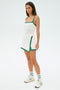 A person in a SPLITS59 Monah Rigor Tank in White/Arugula stands against a plain background. They pair it with white sneakers and socks with green stripes, creating an ideal look for effortlessly transitioning from the court to gym workouts.
