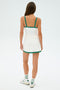 A person wearing the SPLITS59 Monah Rigor Tank in White/Arugula faces away, dressed in a white tennis outfit with green trim. They're also in white sneakers and socks with green lettering, set against a plain background.