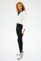 A person with curly hair, wearing a SPLITS59 Joan Fleece Polo Sweatshirt in white with black details, stands against a plain background, paired with black leggings and sneakers.