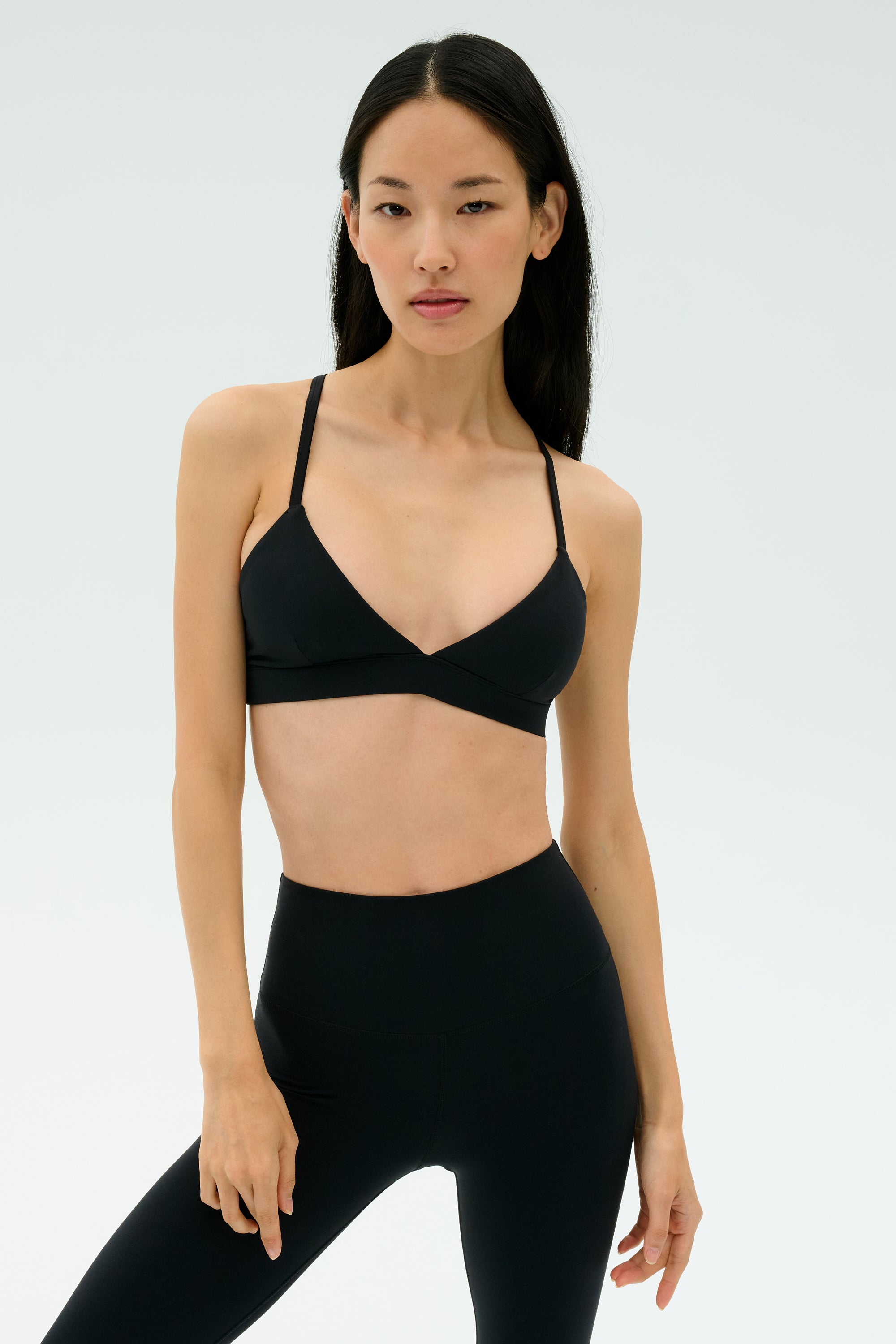 Woman stands against a plain background, wearing the SPLITS59 Theo Rigor Bra - Black and high-waisted black leggings, both crafted from ultra luxe Rigor fabric for multi-sport performance.