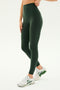 A person wearing SPLITS59's Airweight Super High Waist 7/8 leggings in Military and white running shoes stands against a plain background.