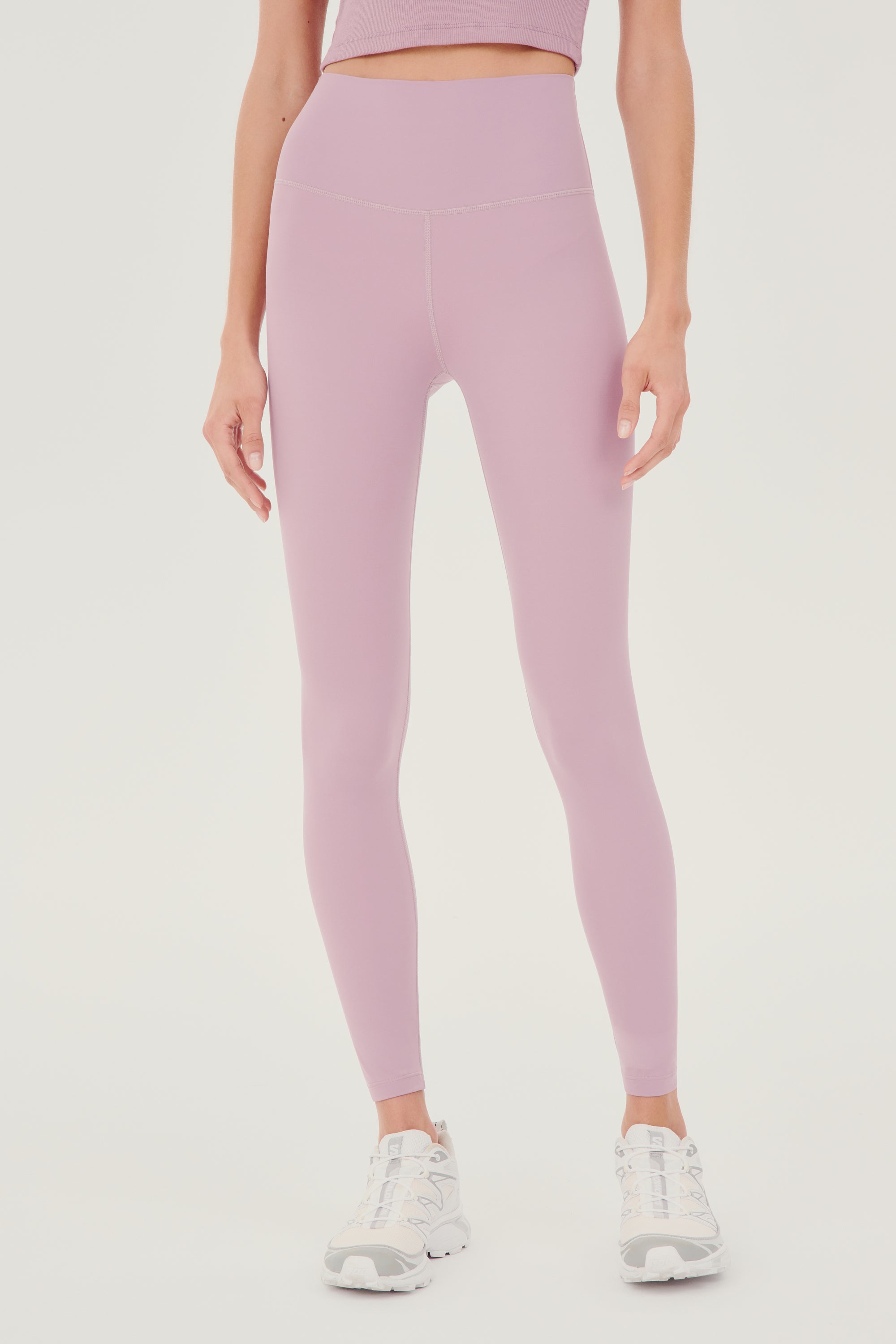 Front view of woman with straight dark hair wearing light pink high waist legging and light pink bra tank paired with white shoes