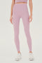 Front view of woman with straight dark hair wearing light pink high waist legging and light pink bra tank paired with white shoes