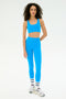 A woman wears the SPLITS59 Ella High Waist Airweight 7/8 leggings in Riviera/White, paired with a matching sports bra, white socks with black stripes, and white sneakers against a plain white background.