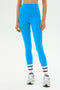 Someone wearing SPLITS59 Ella High Waist Airweight 7/8 leggings in Riviera/White, paired with white athletic shoes and white socks with blue stripes, stands against a simple light background.