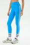 Model wears SPLITS59 Ella High Waist Airweight 7/8 leggings in Riviera/White with white socks and gray sneakers, standing against a plain white background.