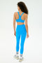 A person with curly hair, wearing the SPLITS59 Ella High Waist Airweight 7/8 leggings in Riviera/White, faces away against a plain light background.