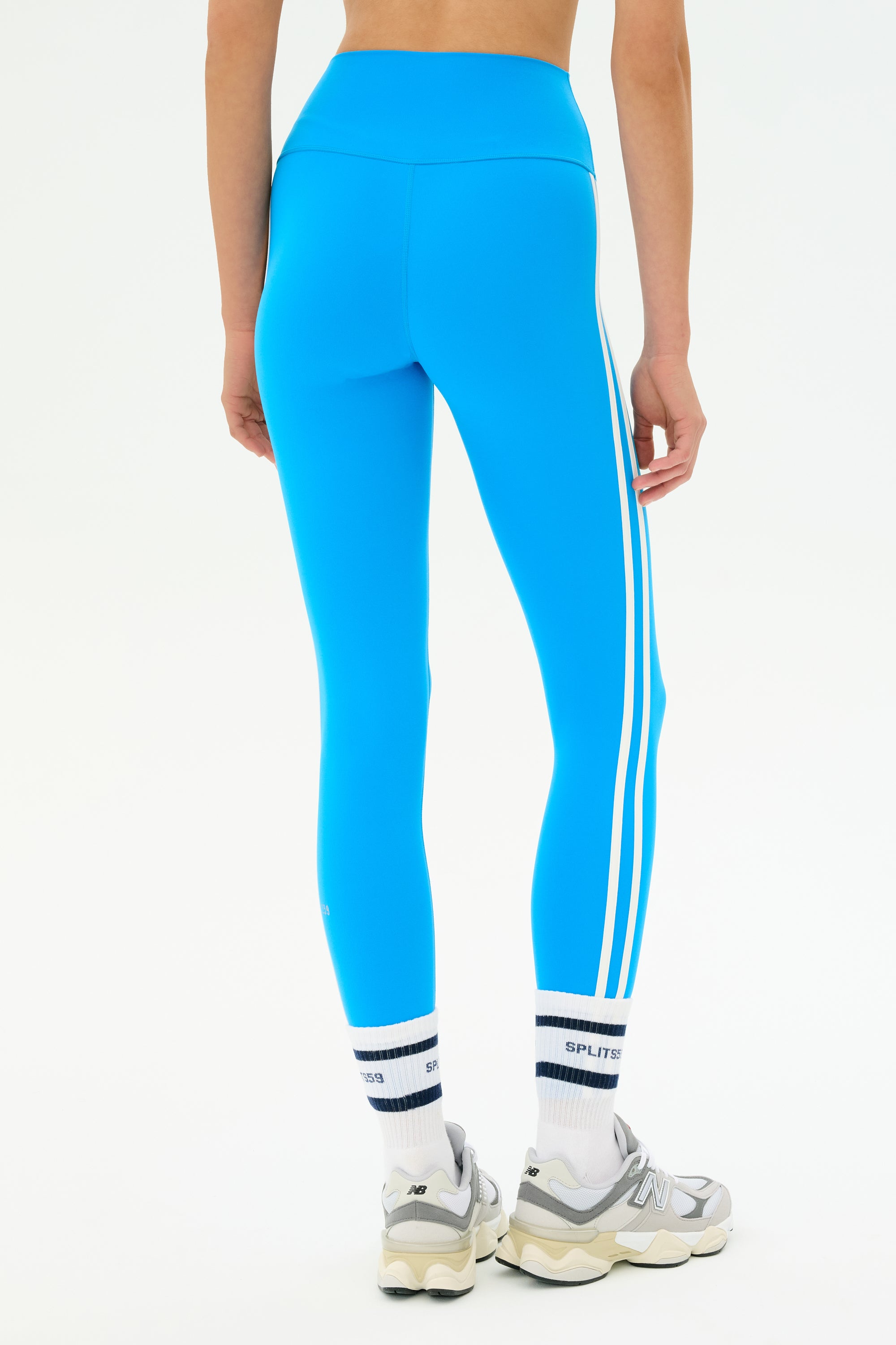 Someone wears SPLITS59 Ella High Waist Airweight 7/8 leggings in Riviera/White, paired with white socks and gray sneakers, standing against a plain white background.