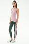 A woman poses against a plain background in the SPLITS59 Kiki Rib Tank Full Length - Blush, paired with green leggings featuring pink spandex stripes and white athletic shoes.