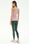 A woman stands facing away, wearing the SPLITS59 Kiki Rib Tank Full Length in Blush and dark green leggings with a pink side stripe, paired with white sneakers, against a plain white background.