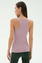 A woman stands facing away, wearing the SPLITS59 Kiki Rib Tank Full Length in Blush, featuring a sleeveless ribbed design crafted from soft modal fabric, paired with dark green leggings against a plain light background.