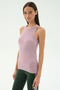 A woman wears the SPLITS59 Kiki Rib Tank Full Length in Blush with dark green spandex leggings, standing against a plain white background.