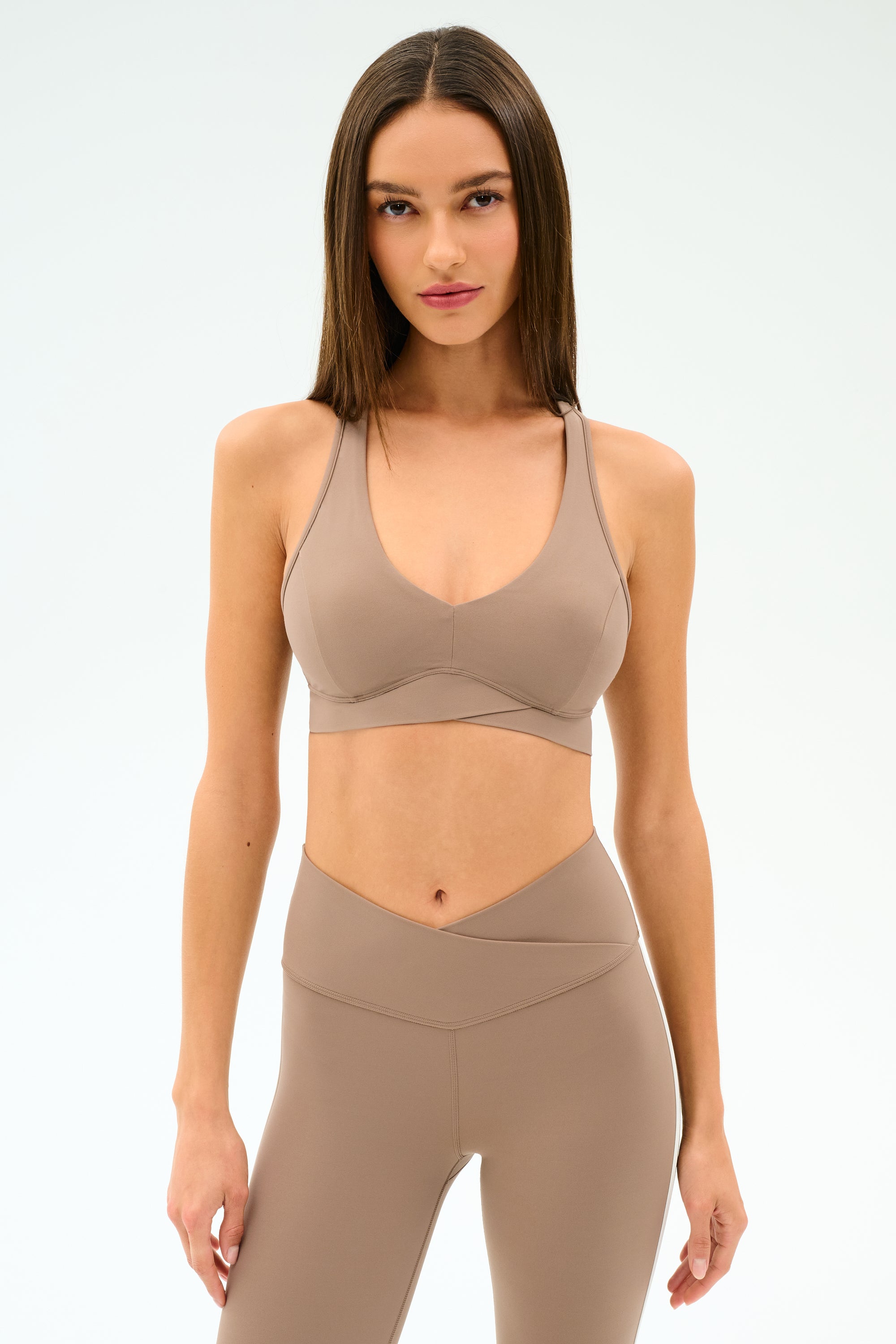 A woman faces forward in a taupe SPLITS59 Mia Rigor Bra - Latte and matching high-waisted leggings, set against a plain light background.
