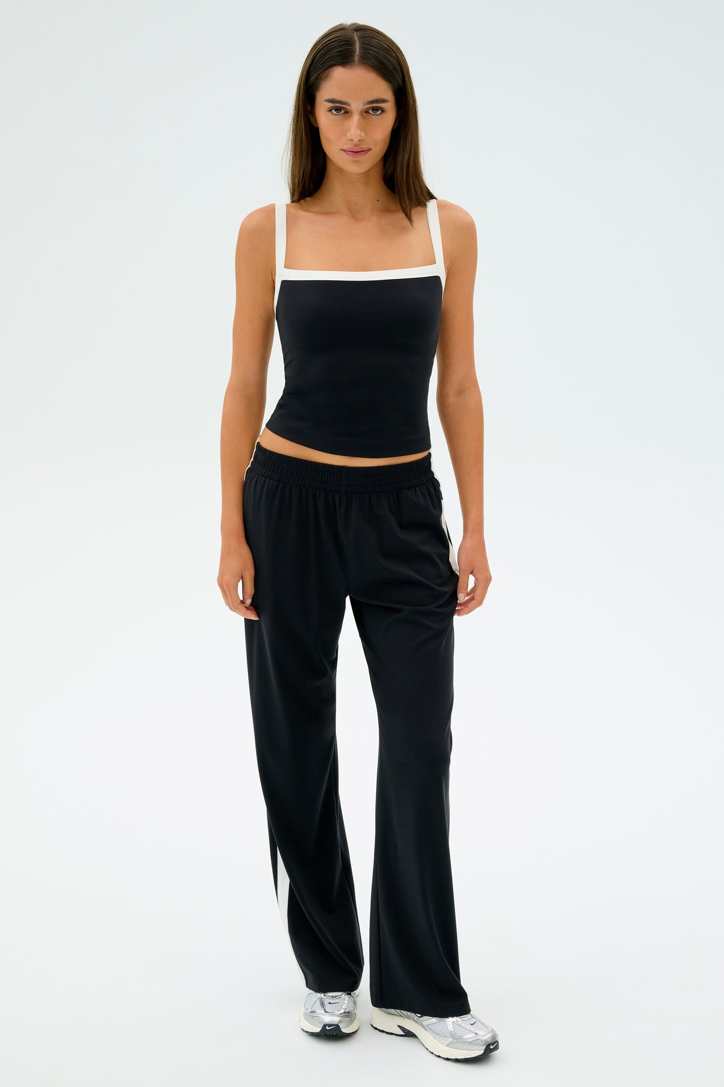 Against a plain background, a person wears the SPLITS59 Monah Rigor Tank in Black/White, paired with black pants and silver sneakers.