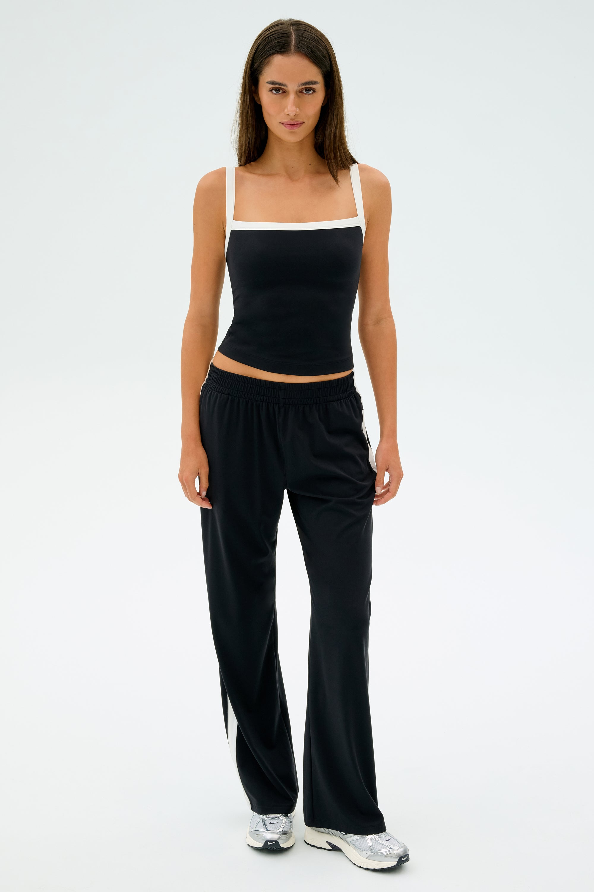 Against a plain background, a person wears the SPLITS59 Monah Rigor Tank in Black/White, paired with black pants and silver sneakers.