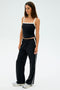A woman poses against a plain white backdrop wearing the SPLITS59 Monah Rigor Tank in Black/White, black pants with white stripes, and silver sneakers.