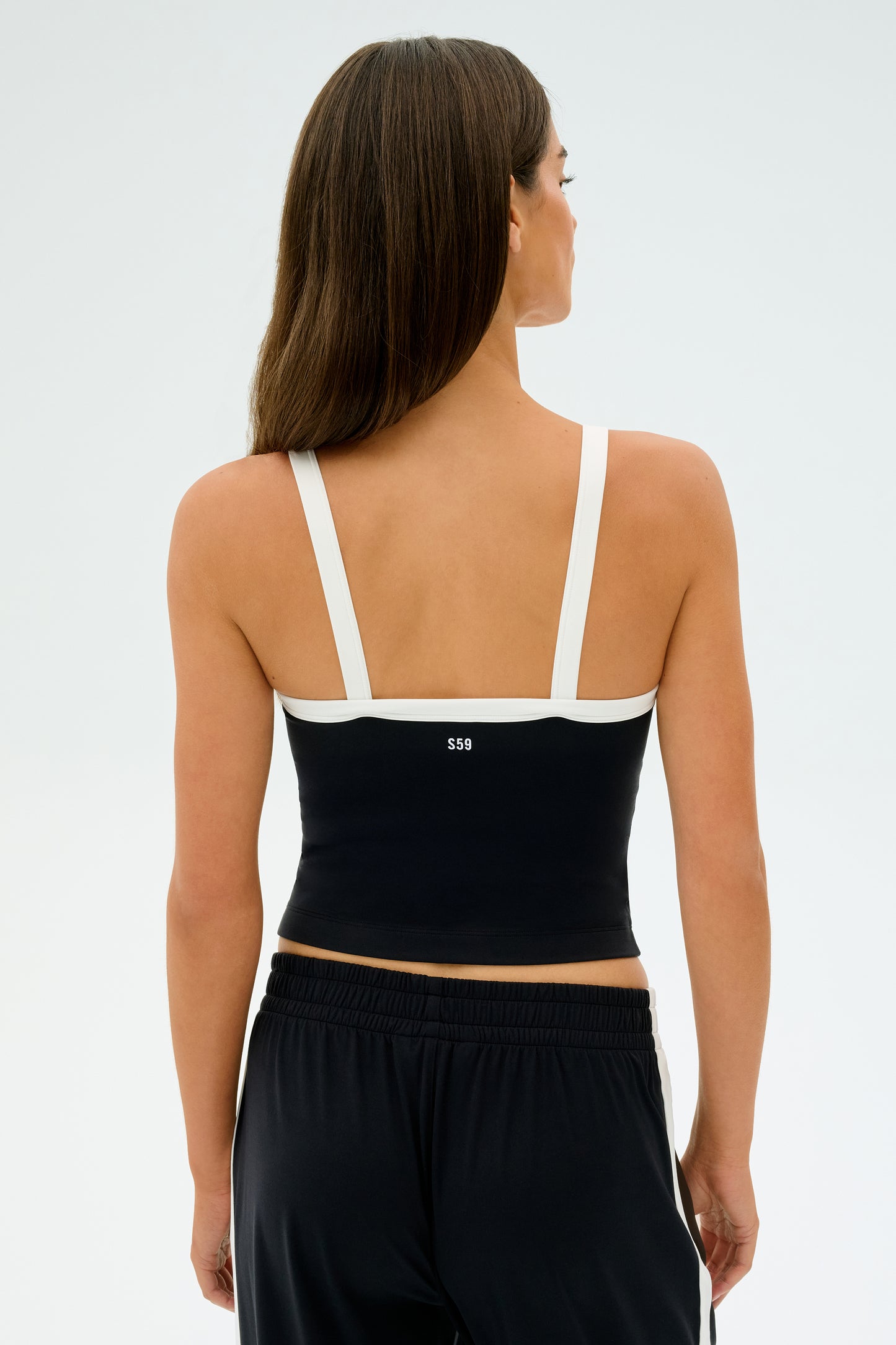 A person with long hair wearing a SPLITS59 Monah Rigor Tank in Black/White and black pants, standing with their back to the camera.