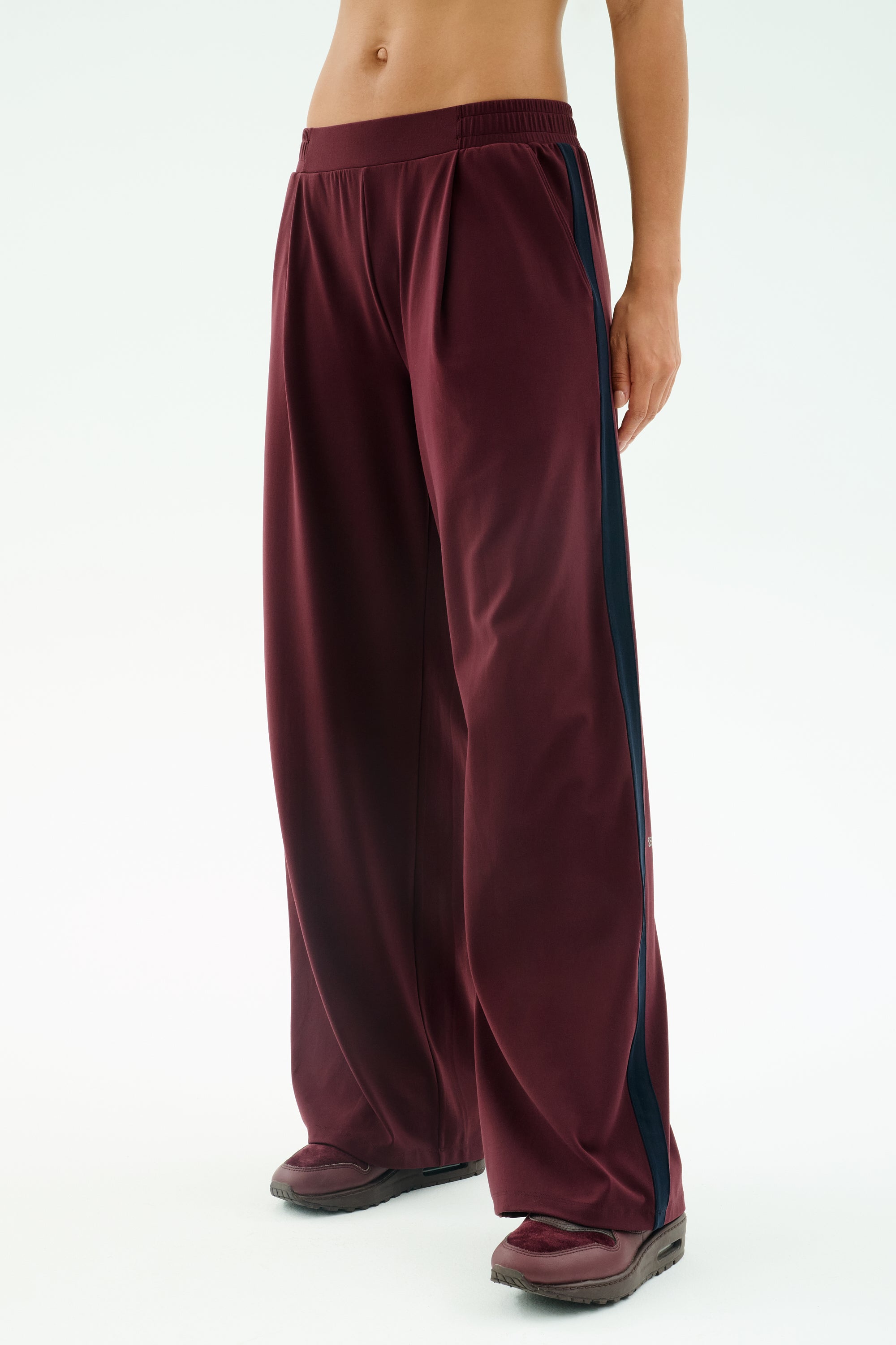 A person wears SPLITS59's Luca Airweight Trouser with Stripe in Dark Cherry/Indigo, paired with black shoes, standing against a plain light background.