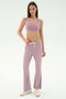 A woman stands against a white background wearing SPLITS59's Blaire Rib Pant in Blush, a coordinating mauve spandex sports bra, and white sneakers.