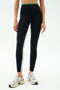 A person wears SPLITS59 Easton Rigor High Waist 7/8 leggings in Black/Grass, featuring a compressive fit and white side stripes for workout support, paired with white running shoes against a plain light background.