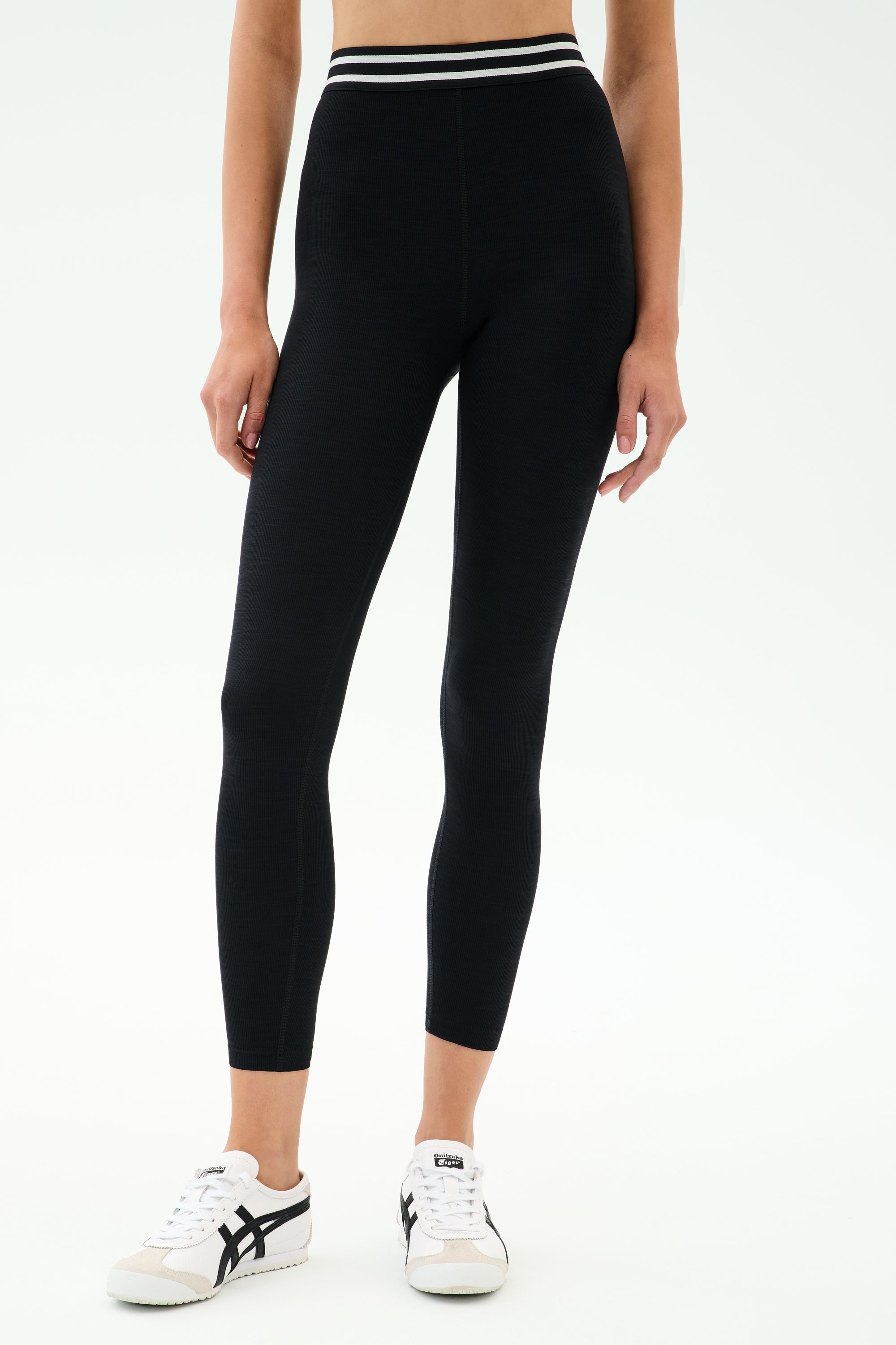 A person wearing SPLITS59’s Bailey High Waist Active Rib 7/8 legging in black with a white striped waistband and white sneakers stands against a plain light background—ideal for gym workouts.