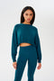 A woman wearing a SPLITS59 Noah Fleece Crop Sweatshirt in Peacock and leggings.