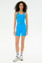 A woman faces forward against a white background, wearing SPLITS59's Ella High Waist Airweight Short in Riviera/White with a matching blue sleeveless top, striped white socks, and sneakers.