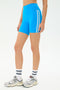 A person wearing SPLITS59 Ella High Waist Airweight Short in Riviera/White, paired with white socks and gray sneakers, stands against a white background.