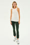 A woman stands facing forward wearing the Kiki Rib Tank Full Length in White by SPLITS59, dark green leggings, and gray athletic shoes against a plain white background, ready for yoga or gym workouts.
